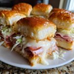 Close-up of cheesy, baked grinder sliders filled with deli meats and shredded lettuce on a white plate.