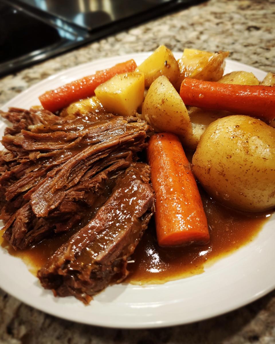 A plate featuring tender, shredded pot roast smothered in gravy alongside cooked carrots and potatoes.