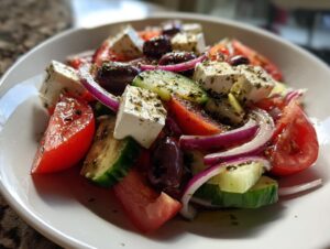 Close-up of a vibrant bowl featuring an authentic greek salad with chunks of feta, red onion, cucumber, tomatoes, and Kalamata olives.
