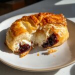 Close-up of a golden brown baked brie in puff pastry cut open to show melted brie cheese and dark berry jam.