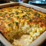 Close-up of a creamy, baked street corn dip in a casserole dish with a golden, cheesy crust and fresh parsley.