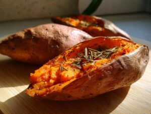 Close-up of a fluffy, split baked sweet potatoes seasoned with pepper and topped with fresh rosemary sprigs.