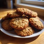 A pile of golden brown, textured banana oatmeal cookies stacked on a white plate.