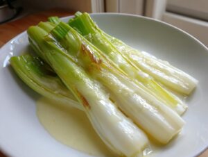 Close-up of tender braised leeks served in a white bowl with a creamy, pale yellow sauce.