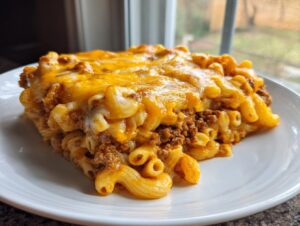 A generous slice of baked cheeseburger casserole featuring elbow macaroni, ground beef, and a thick layer of melted cheddar cheese.