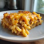 A close-up serving of baked cheeseburger casserole featuring elbow macaroni, ground beef, and a thick layer of melted, browned cheddar cheese.