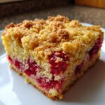 A close-up of a square slice of cherry dump cake with a golden crumble topping and bright red cherries inside.