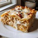 A thick, cheesy slice of chicken alfredo lasagna showing layers of pasta, shredded chicken, and creamy sauce.