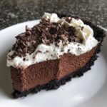 A decadent slice of chocolate mousse pie featuring a dark crust, thick chocolate filling, whipped cream, and chocolate shavings.