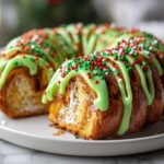 A close-up of festive Christmas tree cinnamon rolls drizzled with bright green icing and covered in red, green, and white sprinkles.
