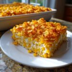 A square slice of rich cream cheese corn casserole topped with golden, crunchy cornflakes, served on a white plate.