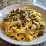 Close-up of fettuccine noodles coated in a rich sauce with ground beef, making up the creamy beef pasta, garnished with fresh parsley.