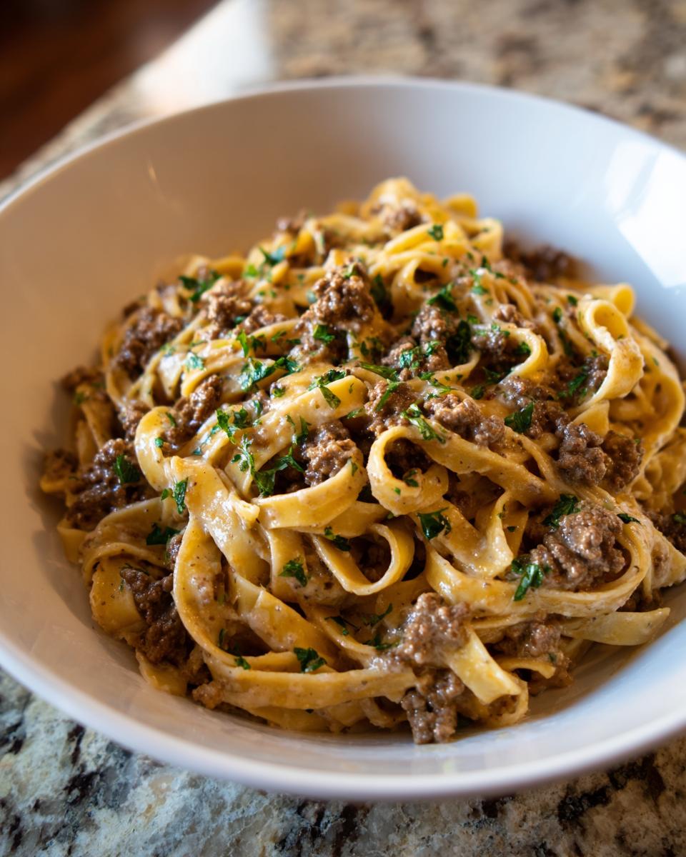 A close-up shot of rich, creamy beef pasta tossed with fettuccine noodles and topped with fresh parsley.
