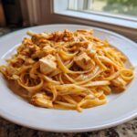 A close-up of creamy cajun chicken pasta featuring fettuccine noodles and chunks of seasoned chicken.
