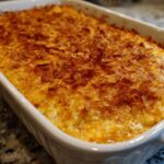 A baked cheesy potato dish in a white casserole dish topped with a golden brown, crunchy cornflake crust.