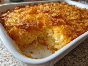 A close-up of a creamy cheesy potato bake in a white dish with a golden, crispy cornflake topping.
