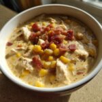 A close-up of a bowl of creamy corn chowder recipe, filled with chicken, corn kernels, and topped generously with crumbled bacon.