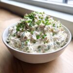 A white bowl filled with creamy clam dip, generously topped with fresh chopped green chives.