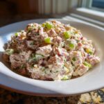 A close-up of a creamy ham salad recipe, featuring diced ham, celery, and red onion, served in a white bowl.