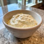 A white bowl filled with thick, creamy horseradish sauce speckled with black pepper, sitting on a granite countertop.