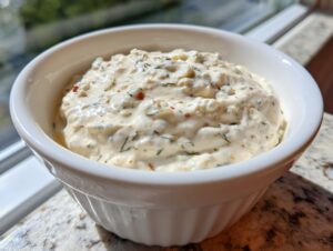 A close-up of thick, textured creamy horseradish sauce mixed with herbs and spices in a small white bowl.