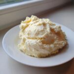 A generous scoop of incredibly creamy mashed potatoes piled high on a small white plate, ready to eat.