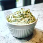 Close-up of creamy, dill-flecked pickle dip served in a small white ruffled bowl on a marble counter.