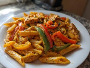A serving of vibrant Rasta pasta featuring penne coated in a creamy sauce, mixed with sliced red, green, and yellow bell peppers and chicken pieces.