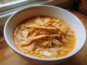 A close-up of creamy tortilla soup filled with shredded chicken and topped generously with crispy tortilla strips.