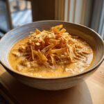 A close-up of a bowl of creamy tortilla soup topped generously with crispy fried tortilla strips.