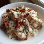 Close-up of shredded chicken in a creamy sauce with sun-dried tomatoes and parsley, representing crockpot marry me chicken.