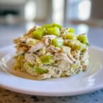 A molded serving of creamy dill pickle chicken salad, featuring shredded chicken, chopped pickles, and topped with bright green celery chunks.