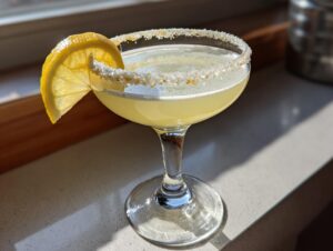 A bright, chilled lemon drop martini in a coupe glass with a sugar-rim and lemon wheel garnish.
