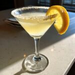 A bright yellow lemon drop martini in a stemmed glass with a sugar rim and lemon wheel garnish.