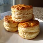 A close-up stack of three tall, fluffy buttermilk biscuits with golden brown tops.
