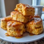 A stack of fluffy, orange-hued sweet potato biscuits generously drizzled with a shiny caramel glaze.