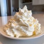 A large, fluffy mound of freshly made vanilla buttercream frosting piled high on a white plate.