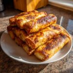 A stack of perfectly cooked, golden brown egg roll appetizers piled high on a white plate.