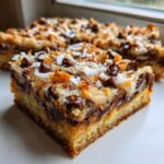 A close-up, gooey slice of magic cookie bars showing a thick crust topped with melted chocolate chips and shredded coconut.
