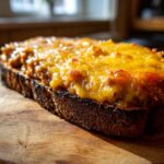 Close-up of a slice of dark toast topped with a thick layer of bubbling, melted orange cheese mixture for the hanky panky recipe.