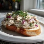 A generous serving of healthy tuna salad with red onion and dill on a slice of toasted bread.