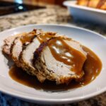 Four slices of juicy instant pot turkey breast seasoned and covered in rich brown gravy, served on a white plate.