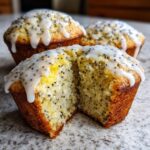 A lemon poppy seed muffin cut in half showing the moist crumb texture, topped with white glaze and poppy seeds.