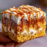 Close-up of a moist slice of pumpkin poke cake topped with cream cheese frosting, caramel sauce, and crumbs.