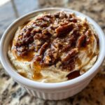 A close-up of creamy no-bake pecan pie dip topped generously with glazed pecans and caramel sauce in a white ramekin.