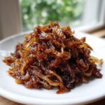 A close-up of a mound of rich, dark brown caramelized onions piled high on a small white plate.