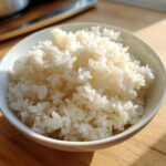 Close-up of perfectly cooked, sticky white sushi rice piled high in a small white bowl.