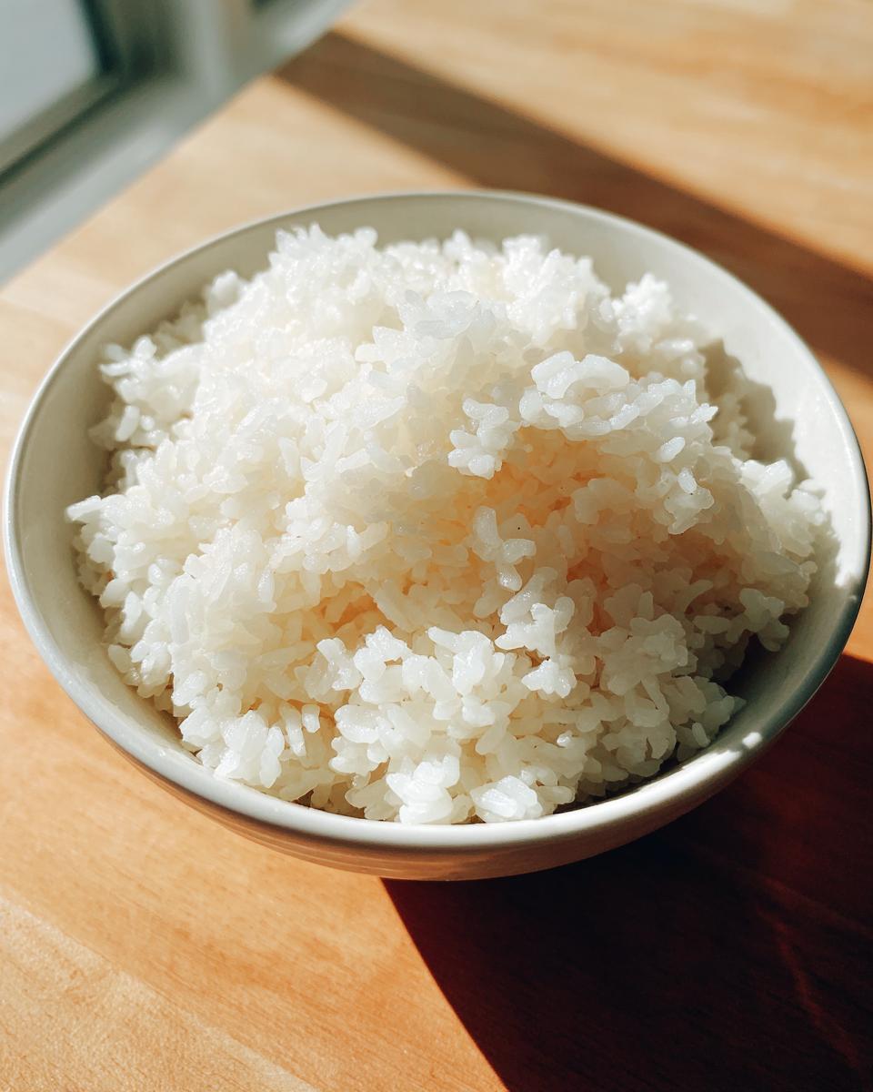 Close-up of perfectly fluffy, white sushi rice mounded in a light-colored bowl on a wooden surface.