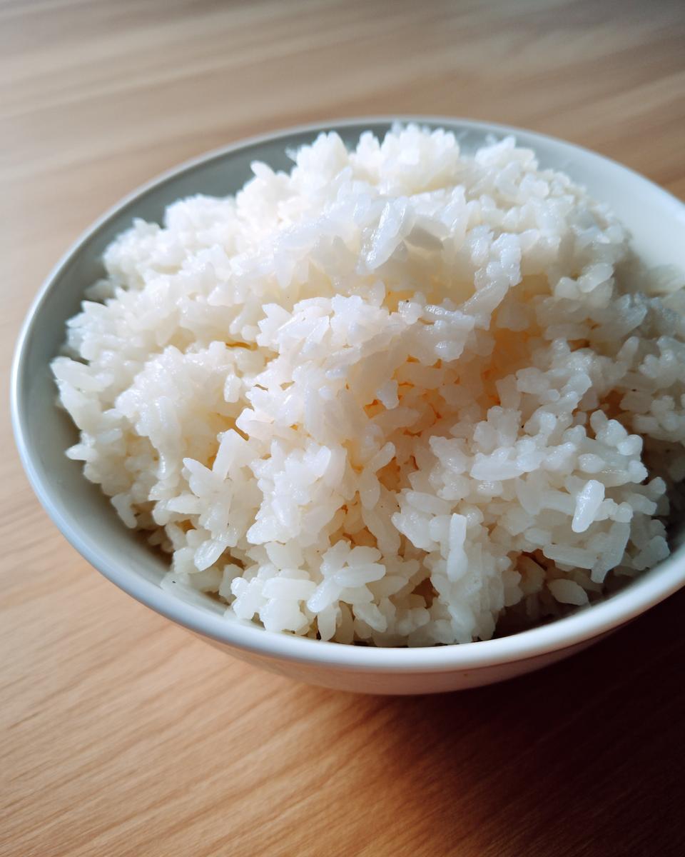 Close-up of fluffy, perfectly cooked white sushi rice in a simple white bowl on a wooden surface.