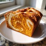 A close-up of a freshly baked pumpkin cream cheese bread loaf showing the vibrant orange color and cream cheese swirl.